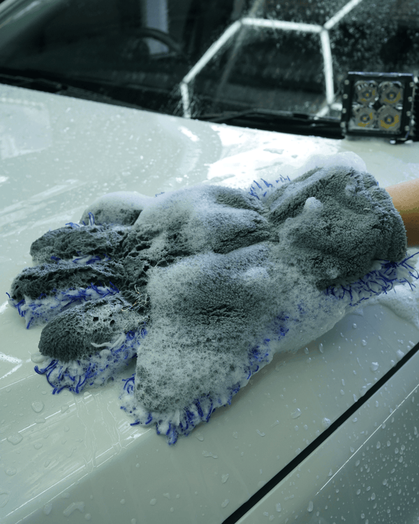 A person washing a white car bonnet with a 5 finger microfibre wash mitt.