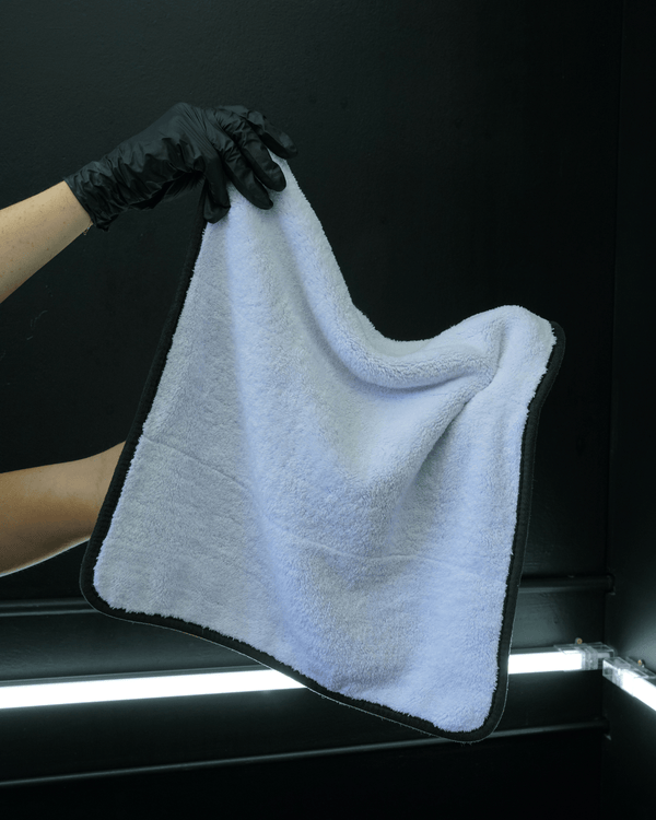 A person holding a white microfibre cloth wearing black gloves on a black background