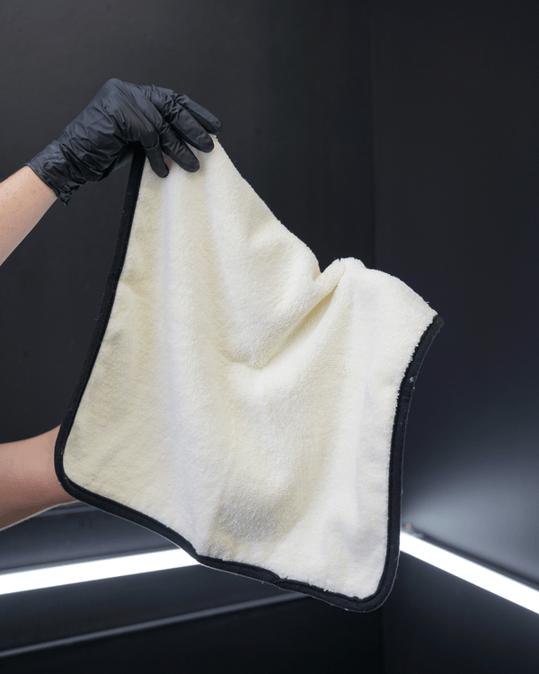 A person wearing black gloves holding a small plush white microfibre cloth