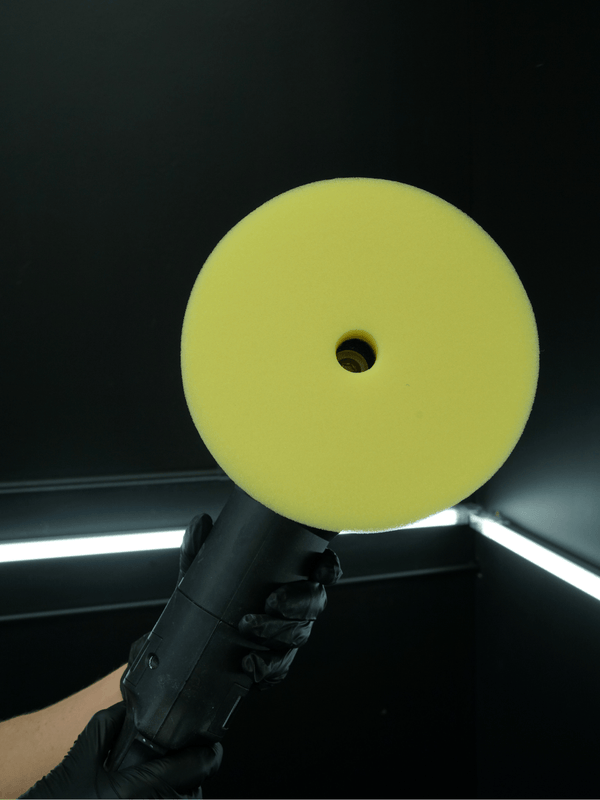 Yellow buffer pad held by a gloved hand against a dark background