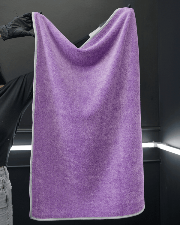 A person wearing black gloves holding a large purple car drying towel in a dark background