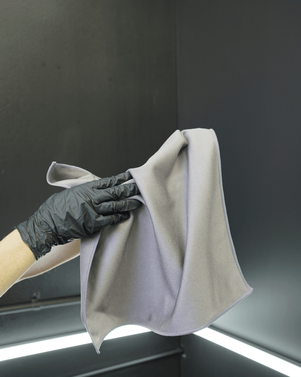 A person wearing black gloves holding a grey glass cloth on a black background