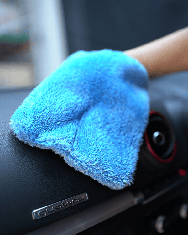 A person holding a blue car interior scrub mitt cleaning a dashboard