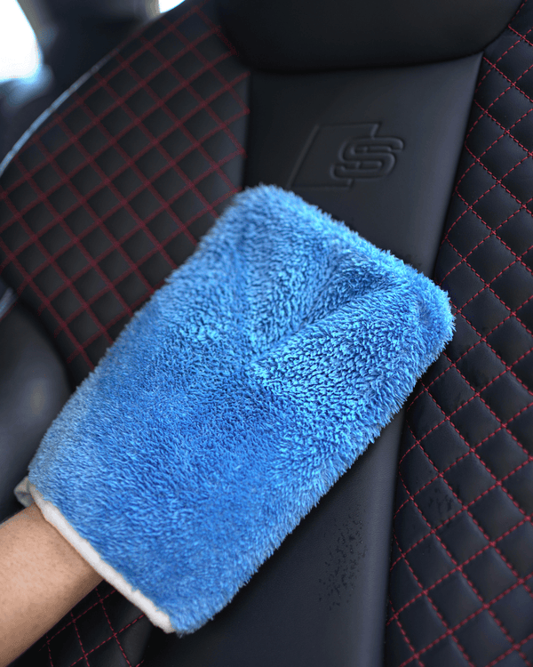 A person holding a car interior scrub mitt cleaning a leather car seat