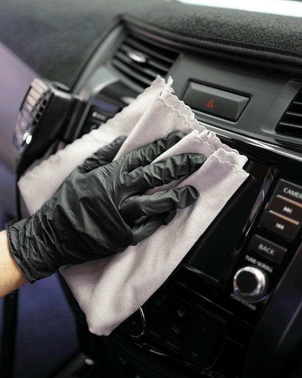A person wearing black gloves cleaning a car screen with a grey suede microfibre cloth