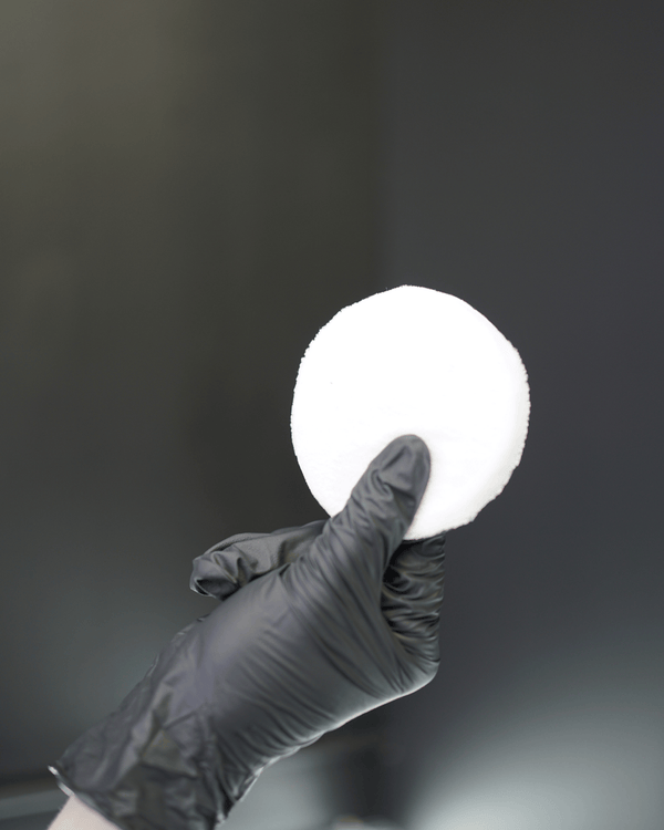 A detailer wearing black gloves with a small white applicator