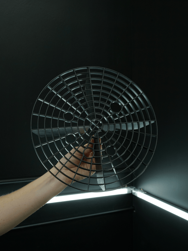 Hand holding a round metal grid against a dark background