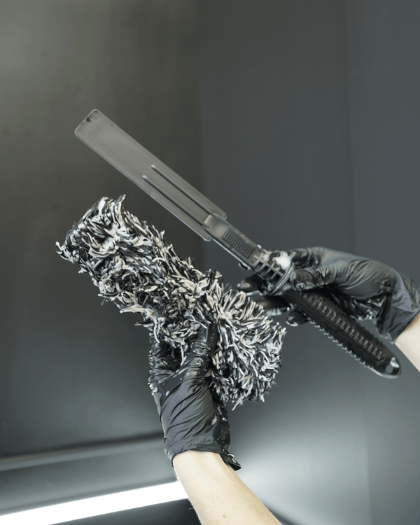 A person with black gloves on holding p a black and white microfibre wheel woolie tyre cleaning tooll