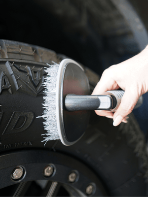 A curved tyre brush being used to clean a car tyre