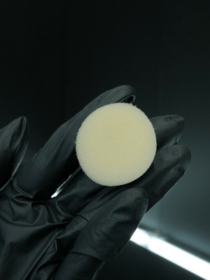 Black glove holding a white circular buffing pad against a dark background