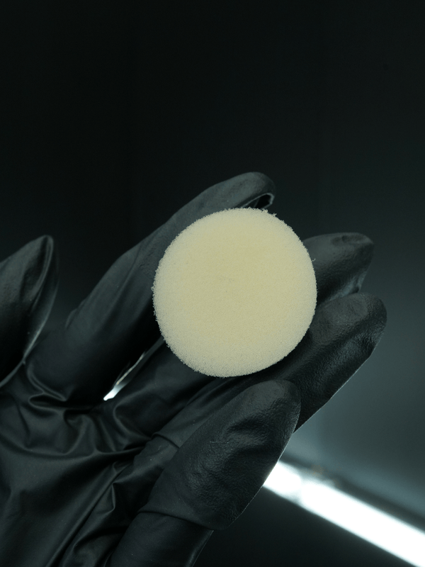 Black glove holding a white circular buffing pad against a dark background