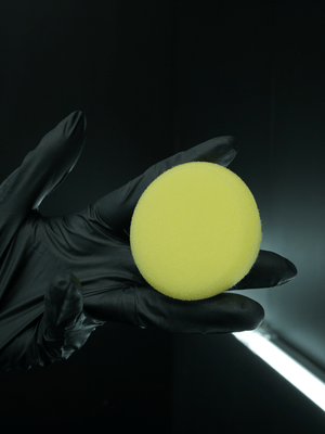 Yellow buffing pad held in a black gloved hand against a dark background