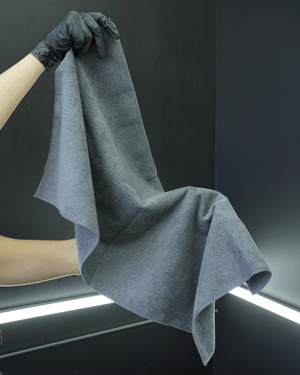 A person with black gloves on holding a large grey microfibre towel 