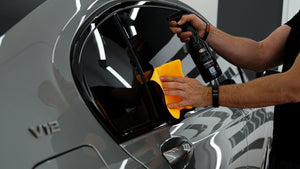 Detailer applying ADBL Hybrid Gloss spray sealant and wiping car side window with yellow microfibre towel