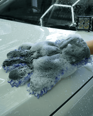 A person washing a white car bonnet with a 5 finger microfibre wash mitt. 