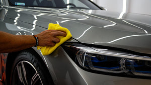 A person wiping a grey BMW with a yellow microfibre cloth