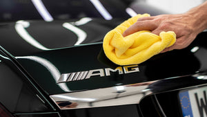 A person wiping a AMG badge with a yellow microfibre cloth
