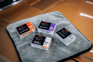 4 boxes of clay bars on a grey towel on a car bonnet