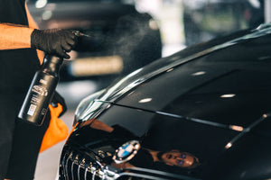 Detailer spraying ADBL Synthetic Spray Wax onto a black BMW hood, applying sealant for high gloss and protection.