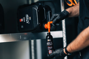 Person refilling 0.2L ADBL CERAMIC QD bottle from a larger black container with an orange spigot