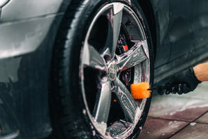 Person cleaning a car wheel and rim with a soapy ADBL Wheel Dagger brush