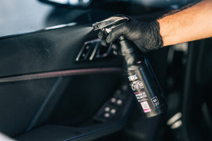 Person spraying ADBL INTERIOR QD onto a textured car door panel and armrest