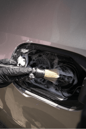 Person cleaning a car's fuel cap with a brush and soapy water.