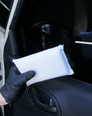 A person wearing a black glove holding a white interior ceramic coating applicator on a black car door