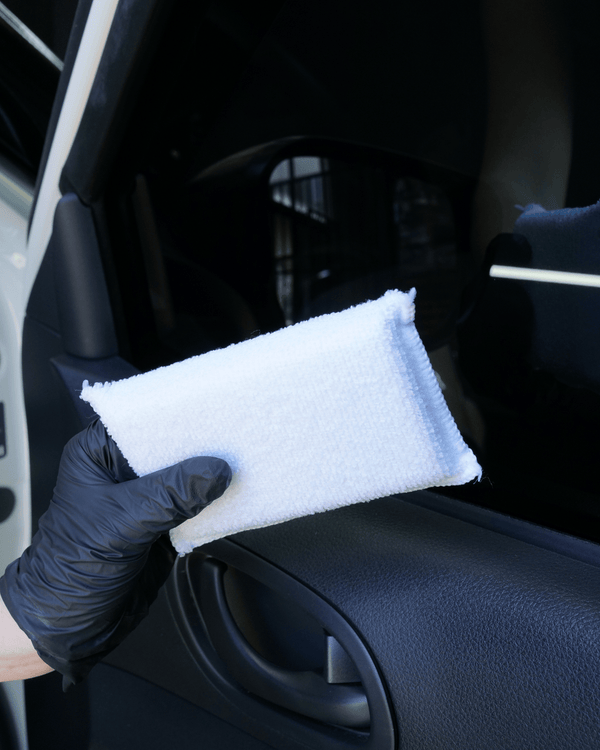 A person wearing a black glove holding a white interior ceramic coating applicator on a black car door