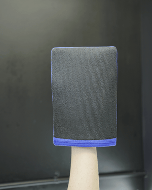 A person holding a blue clay mitt in their hand on a black background