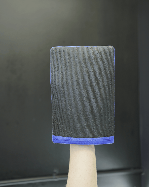 A person holding a blue clay mitt in their hand on a black background