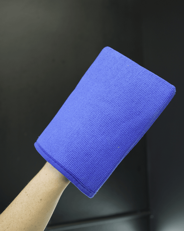 A person holding a blue clay mitt in their hand on a black background