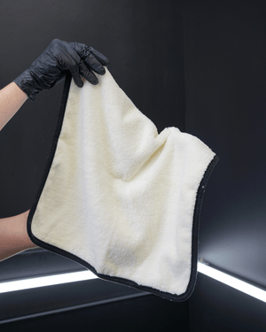 A person wearing black gloves holding a small plush white microfibre cloth