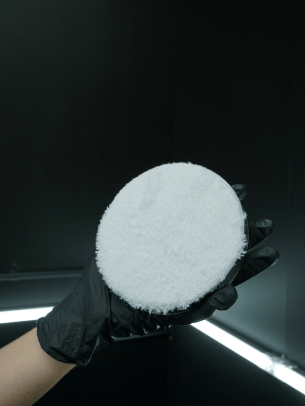 Coral fleece buffing pad on a buffing machine held by a person wearing black gloves against a dark background