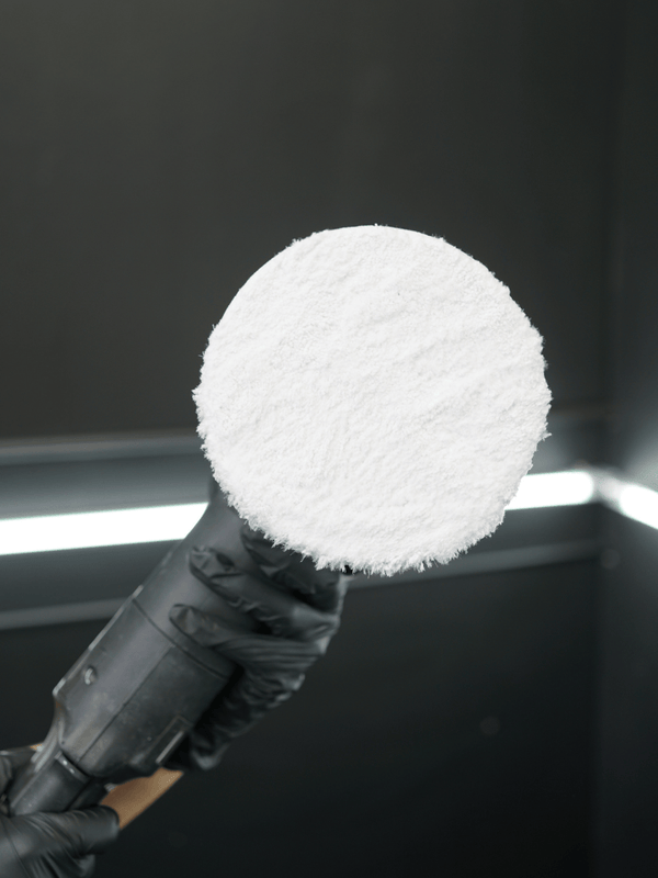 Coral fleece buffing pad on a bufing machine held by a person wearing black gloves against a dark background