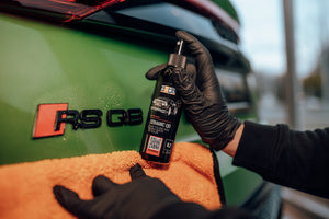 Person in black glove spraying ADBL CERAMIC QD onto a towel near an Audi RS Q8 badge