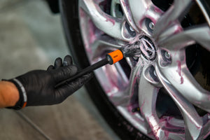 Hand in black glove using ADBL Detail Brush to clean spokes and lug nuts on silver car wheel with chemical