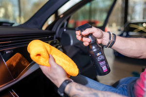 Person applying ADBL INTERIOR QD with a spray bottle and orange microfibre towel to a car dashboard