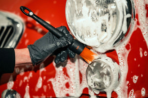Person using DETAILING BRUSH PRO SOFT with car wash foam on a classic red car headlight