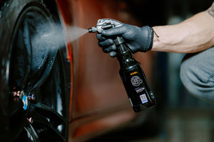 Detailer wearing gloves spraying ADBL Rimtector rim sealant onto a black car wheel/rim.