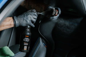Detailer spraying ADBL Leather QD onto a cleaning brush for deep cleaning and conditioning car leather seats.