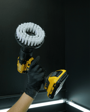 A detailer holding a yellow drill with a carpet drill brush head on it 