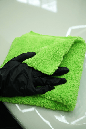 Green microfibre cloth with a black glove on a white car