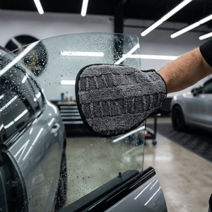 A man using a drying mitt to dry a car window in a detail workshop