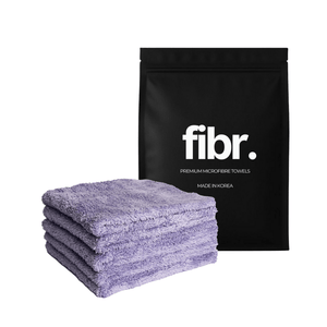 A black bag with FIBR written on it next to a plush purple microfibre cloth stack