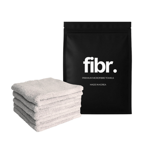 A black bag with FIBR written on it next to a plush 450GSM microfibre cloth stack