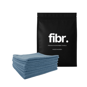 A black bag with FIBR written on it next to a low nap blue microfibre cloth stack