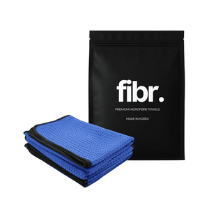 A black bag with FIBR written on it next to a dark blue waffle microfibre drying towel