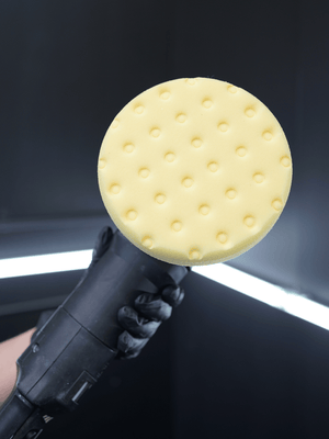 Polishing tool with a yellow pad held against a car window