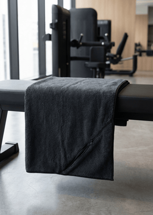 A black gym towel with a zip pocket on a gym bench in a clean minimal gym